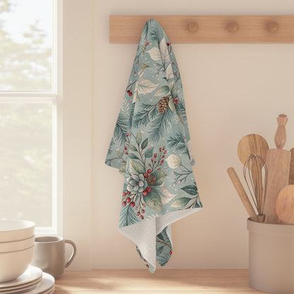 Teal microfiber tea towel with winter foliage, pinecones, and red berries, hanging on a wooden hook.