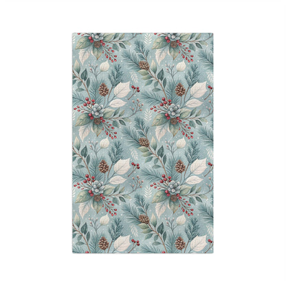 Microfiber tea towel with a repeating winter foliage pattern of teal sprigs, frosted leaves, pinecones, and red berries.