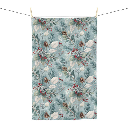Microfiber tea towel with a repeating winter foliage pattern of teal sprigs, frosted leaves, pinecones, and red berries.