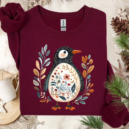 Maroon sweatshirt with a folk art penguin adorned with botanical patterns, flowers, and an orange beak.