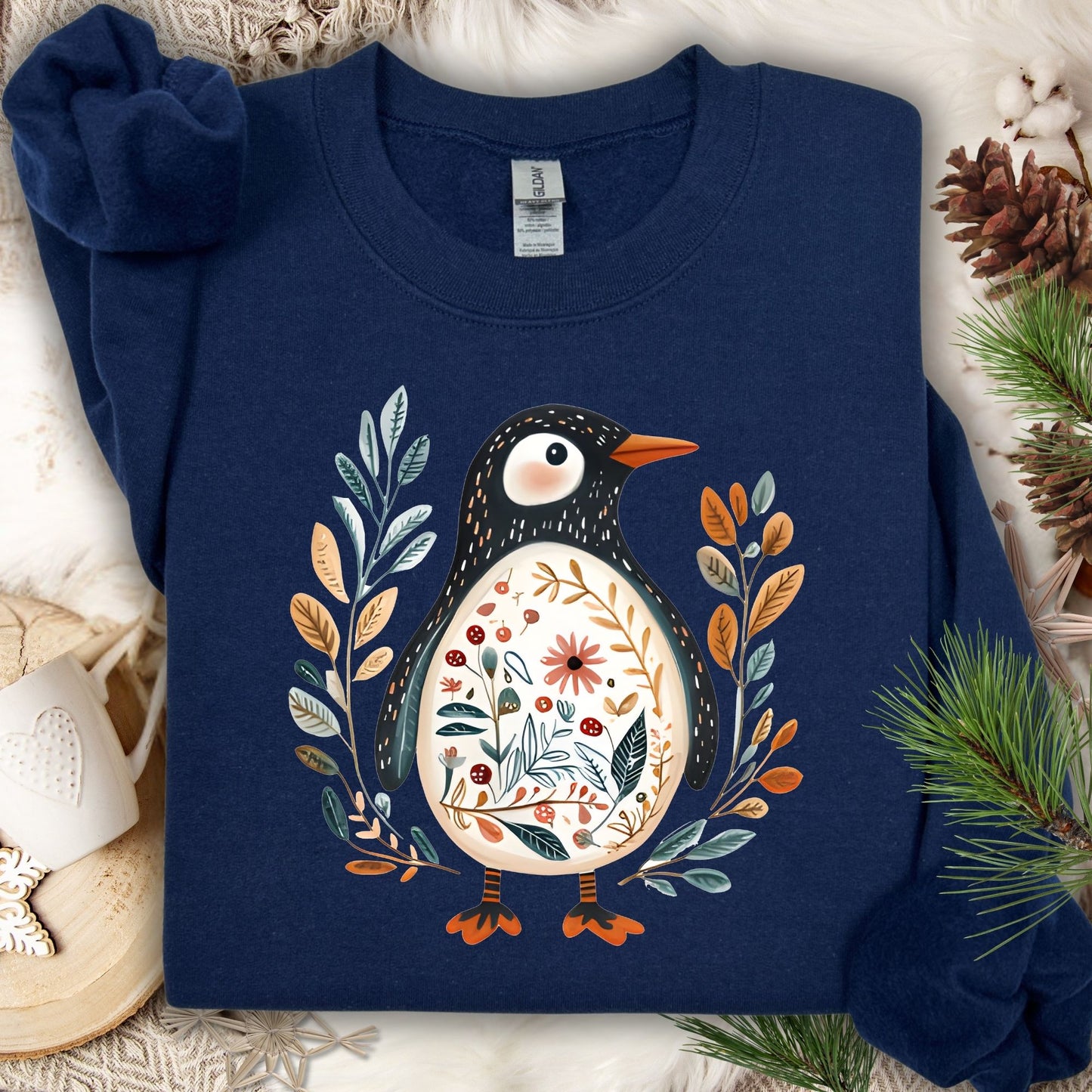 Navy S sweatshirt with folk art penguin, botanical patterns, orange beak, and decorative striped legs.