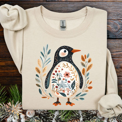 Sand sweatshirt with folk art penguin, botanical patterns, orange beak, and decorative leaves.