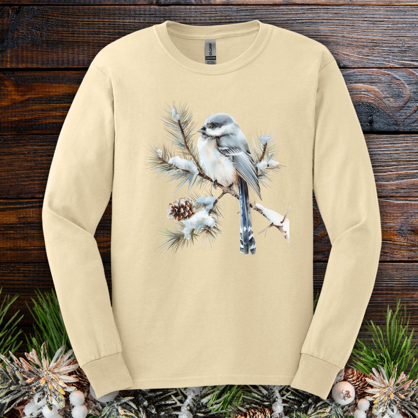Sand long-sleeve tee with watercolor long-tailed tit on snowy evergreen branch.