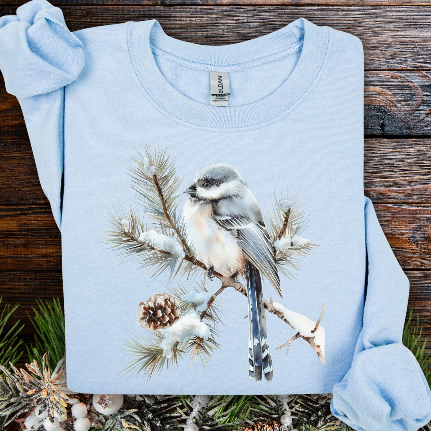 Light blue Gildan S sweatshirt with a watercolor long-tailed tit on a snow-tipped evergreen bough.