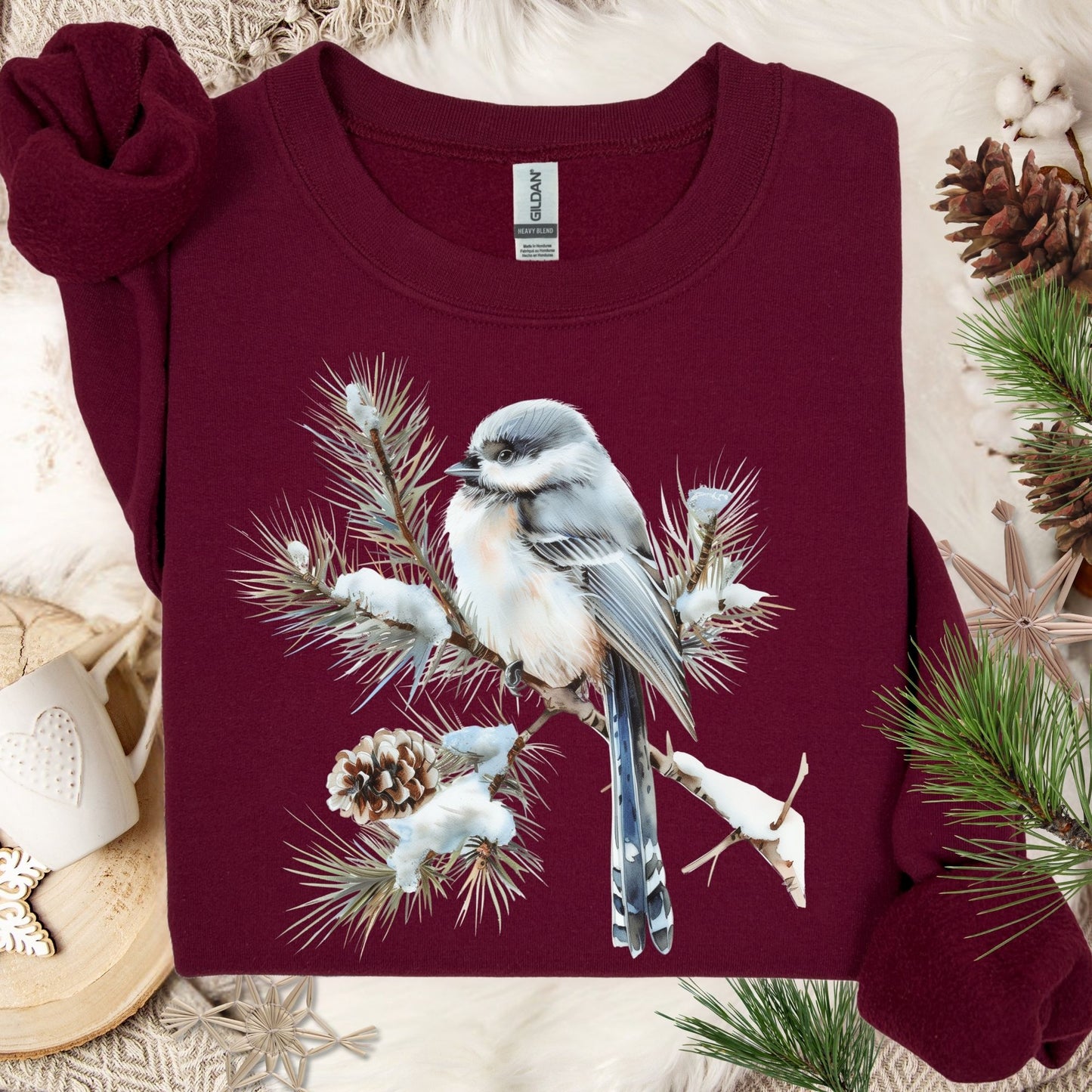 Maroon Gildan sweatshirt with a watercolor long-tailed tit on a snow-tipped evergreen bough.