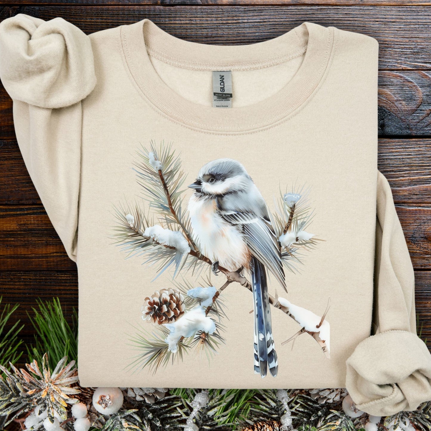 Sand Gildan 18000 sweatshirt with a watercolor long-tailed tit on a snow-tipped evergreen bough.