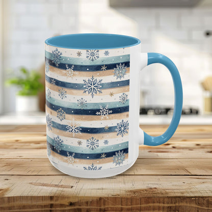 White ceramic mug with blue and beige watercolor stripes, delicate snowflakes, and a contrasting blue interior and handle.
