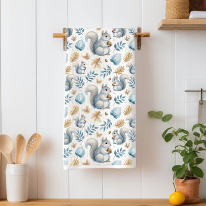 Microfiber tea towel with watercolor squirrels, blue leaves, and ochre sprigs, hanging on a wooden rack.