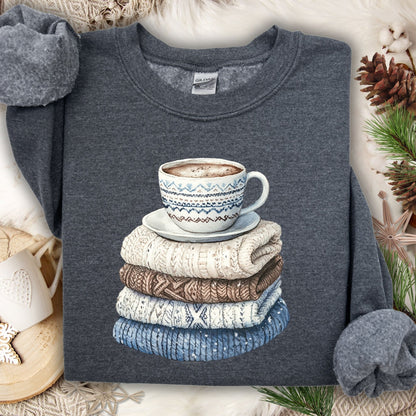 Dark heather sweatshirt with a watercolor-style stack of knit sweaters and a patterned coffee mug.