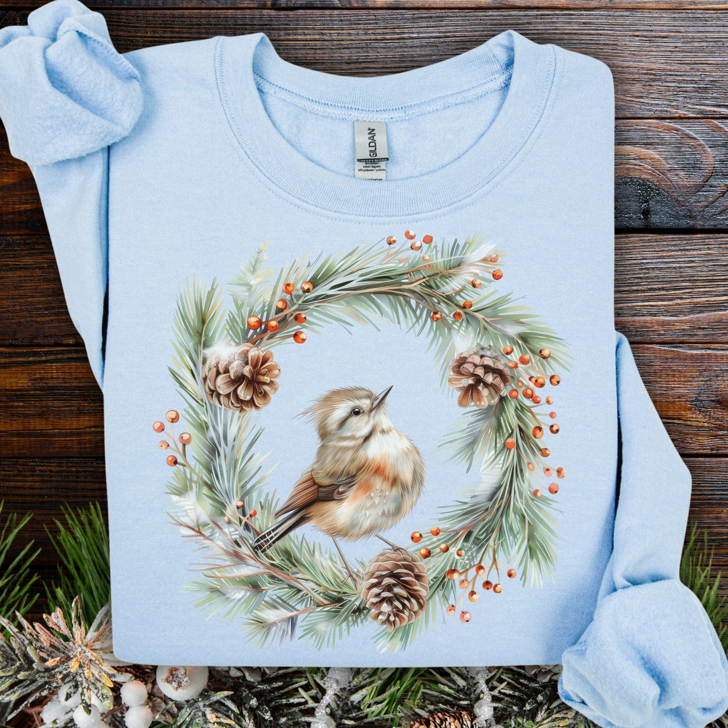 Light blue cotton-polyester sweatshirt with a watercolor wren in an evergreen wreath with pinecones and berries.