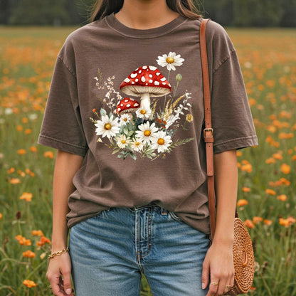Garment-dyed brown t-shirt with a vintage floral mushroom illustration, worn by a person in a meadow.