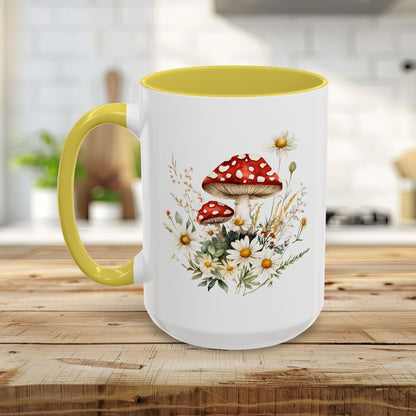 White ceramic mug with yellow handle and interior, featuring a watercolor print of red-capped mushrooms and white daisies.