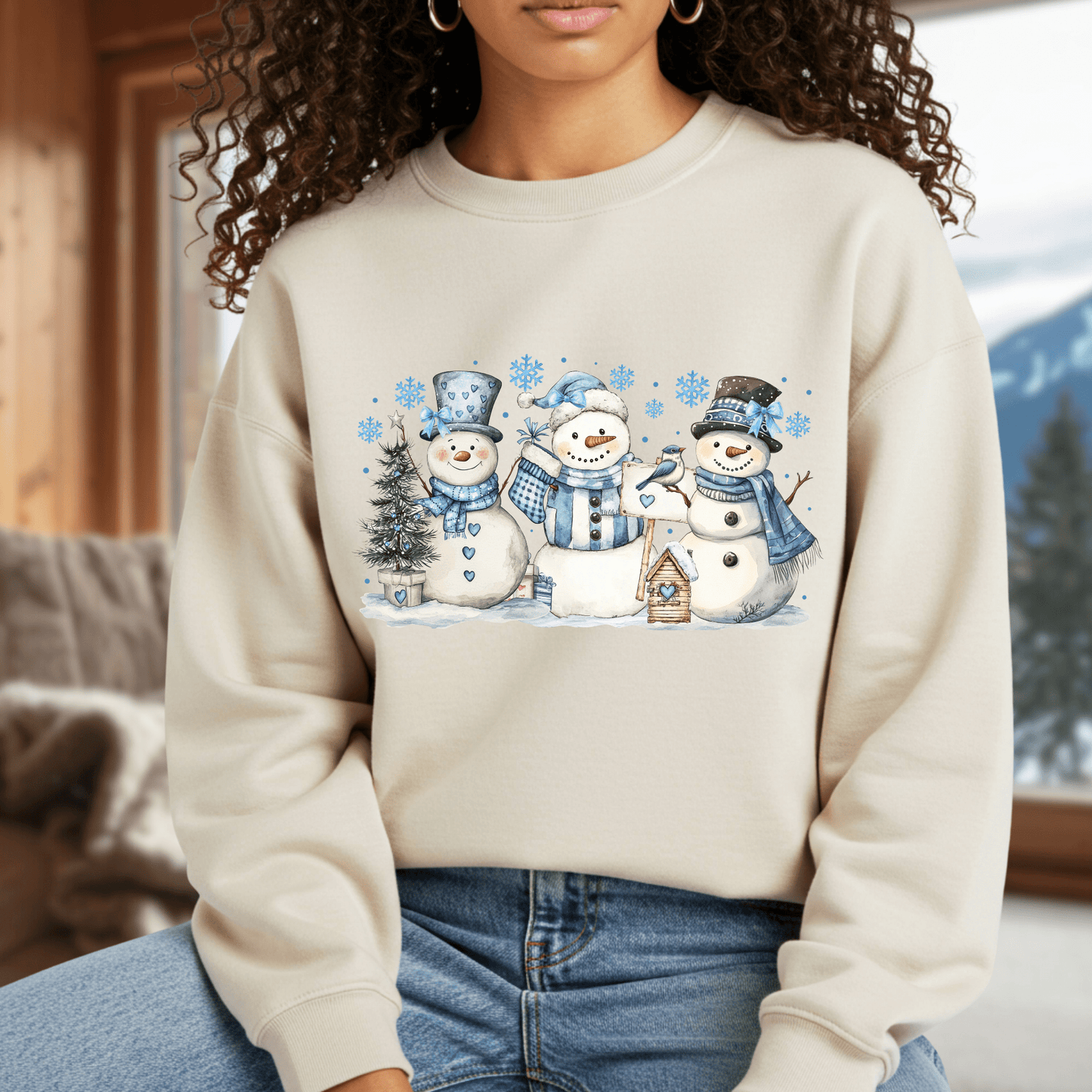 Beige heavy blend sweatshirt with watercolor snowmen, blue hats, scarves, birdhouse, and birds.