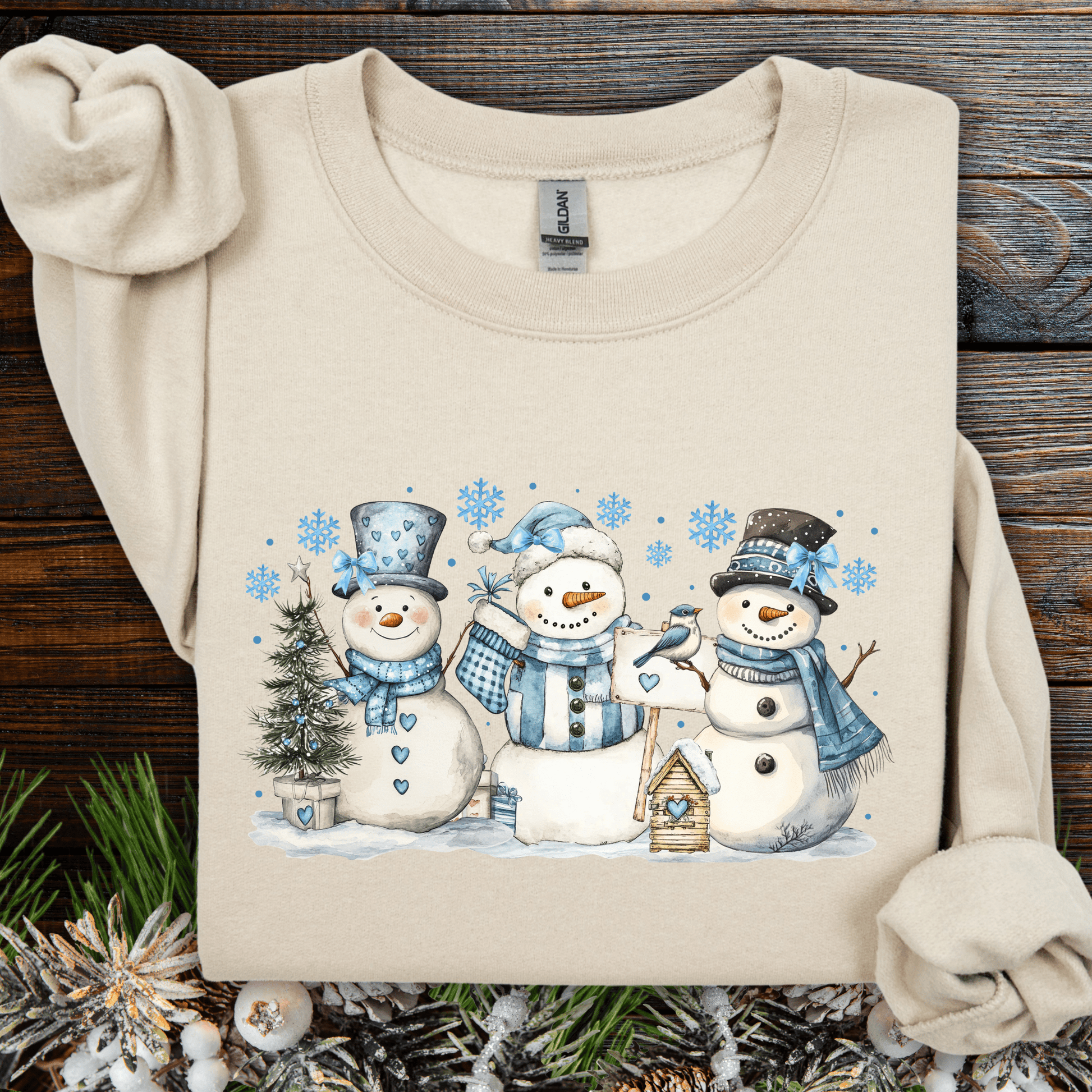 Beige cotton-polyester sweatshirt with watercolor snowmen, blue hats, scarves, birdhouse, and birds.