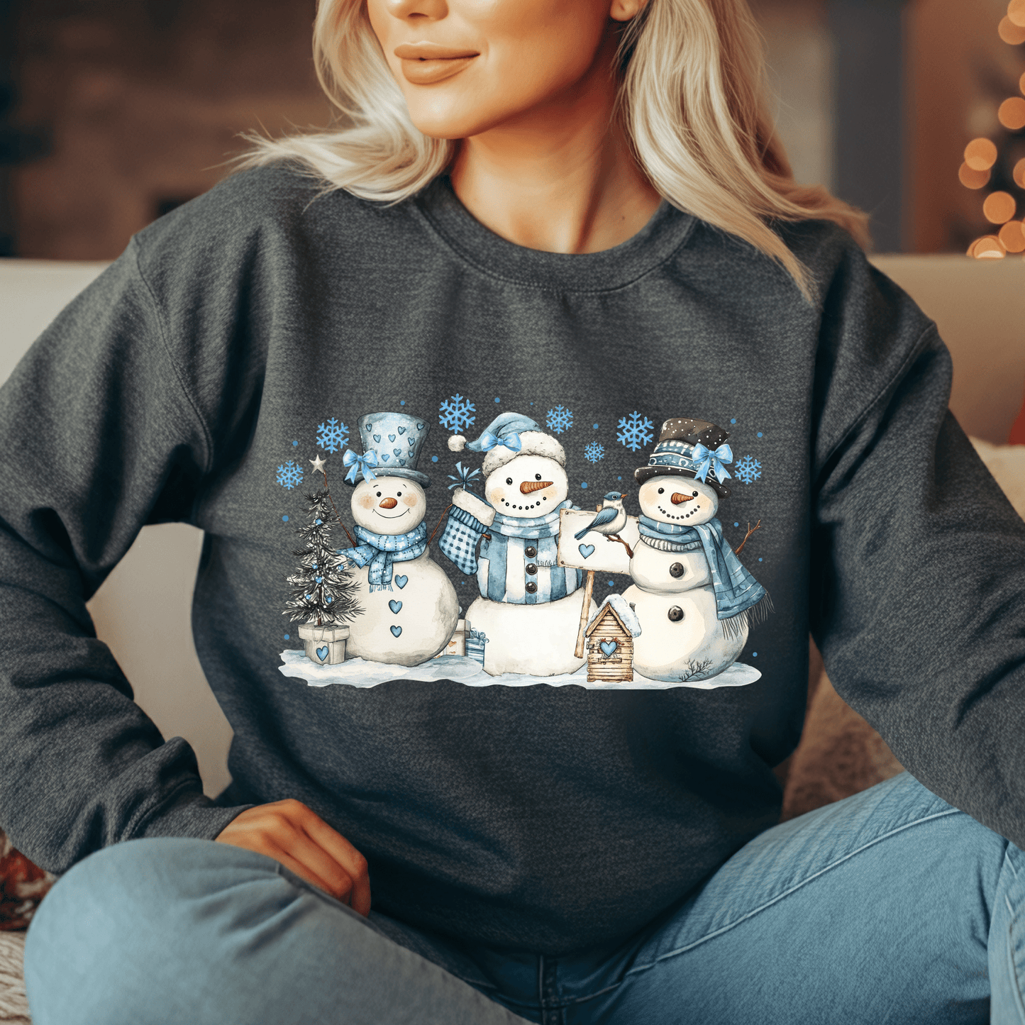 Woman in a charcoal gray sweatshirt with a watercolor design of three snowmen, blue hats, scarves, and birds.