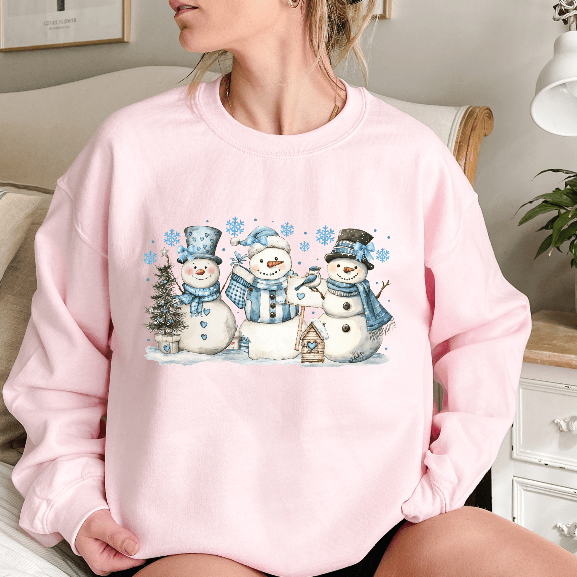 Pink cotton-polyester sweatshirt with watercolor snowmen, blue hats/scarves, birdhouse, and snowflakes.