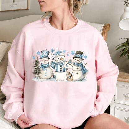 Pink cotton-polyester sweatshirt with watercolor snowmen, blue hats/scarves, birdhouse, and snowflakes.