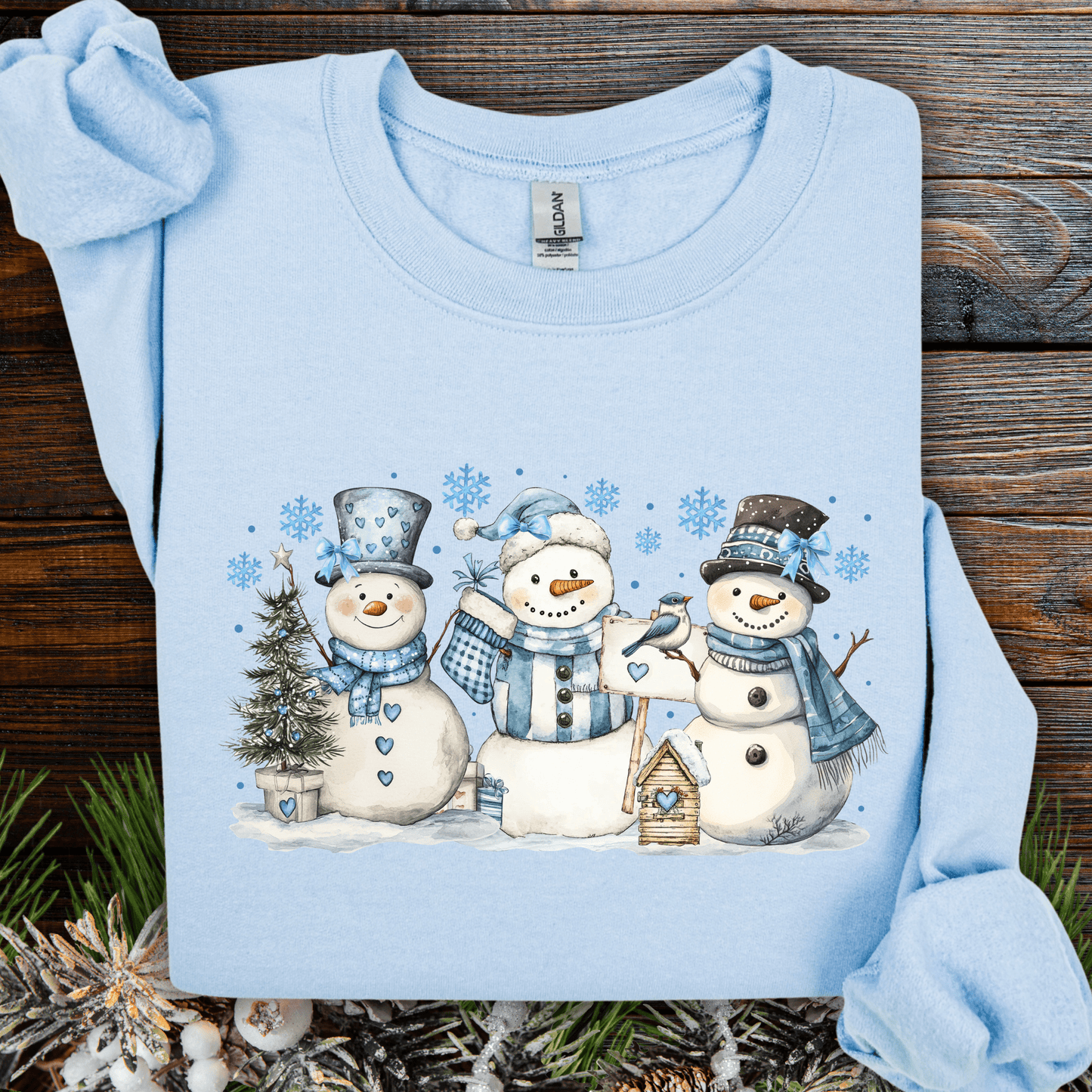 Light blue cotton-polyester sweatshirt with three watercolor snowmen, blue hats, scarves, birdhouse, and birds.