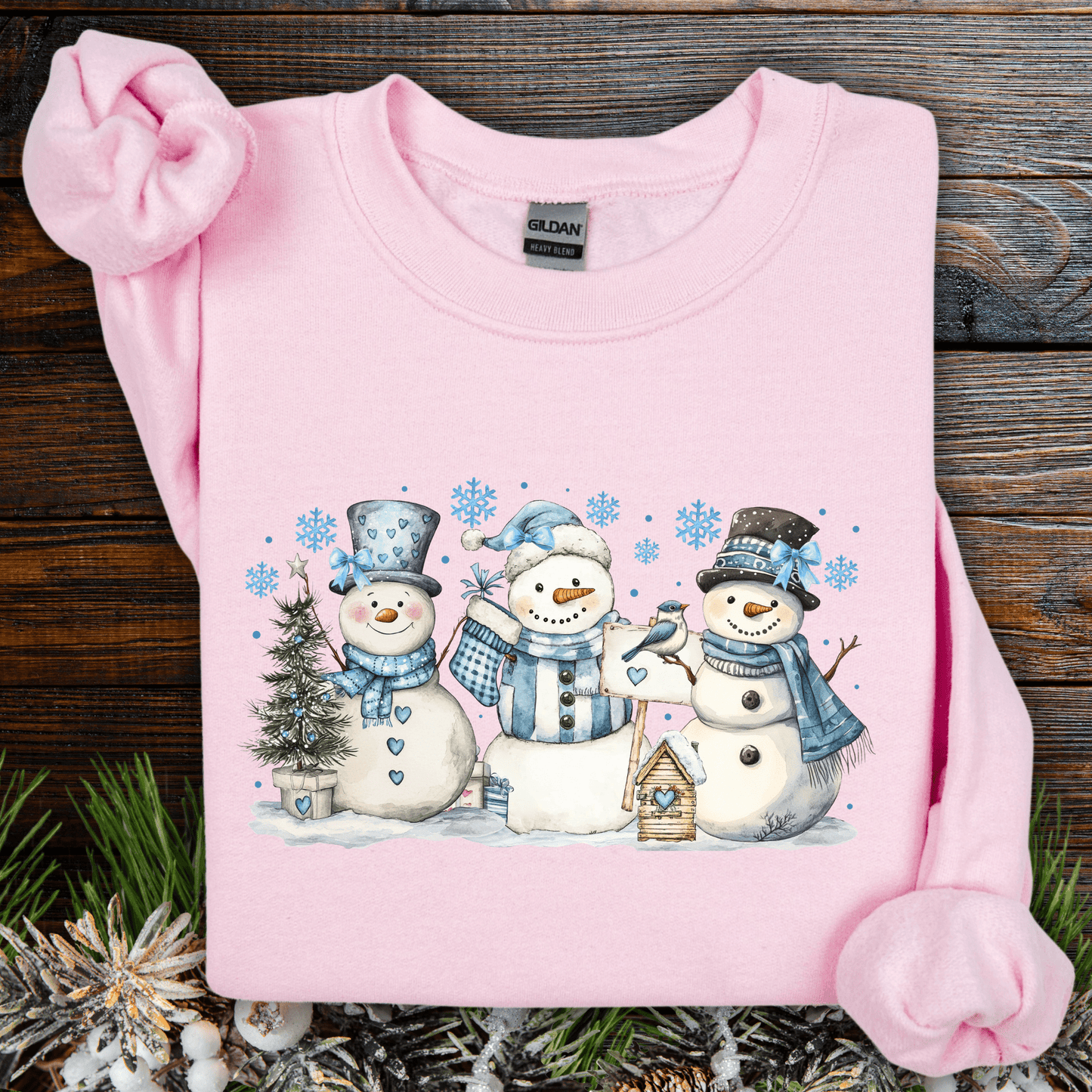 Light pink Gildan sweatshirt with watercolor snowmen, blue hats/scarves, birdhouse, and snowflakes.