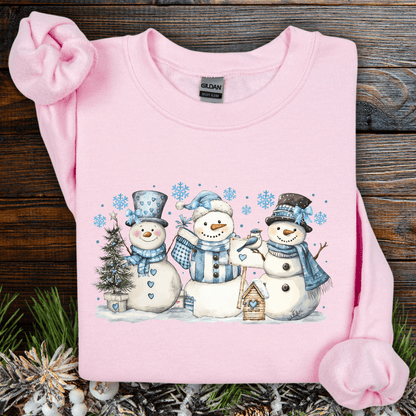 Light pink Gildan sweatshirt with watercolor snowmen, blue hats/scarves, birdhouse, and snowflakes.