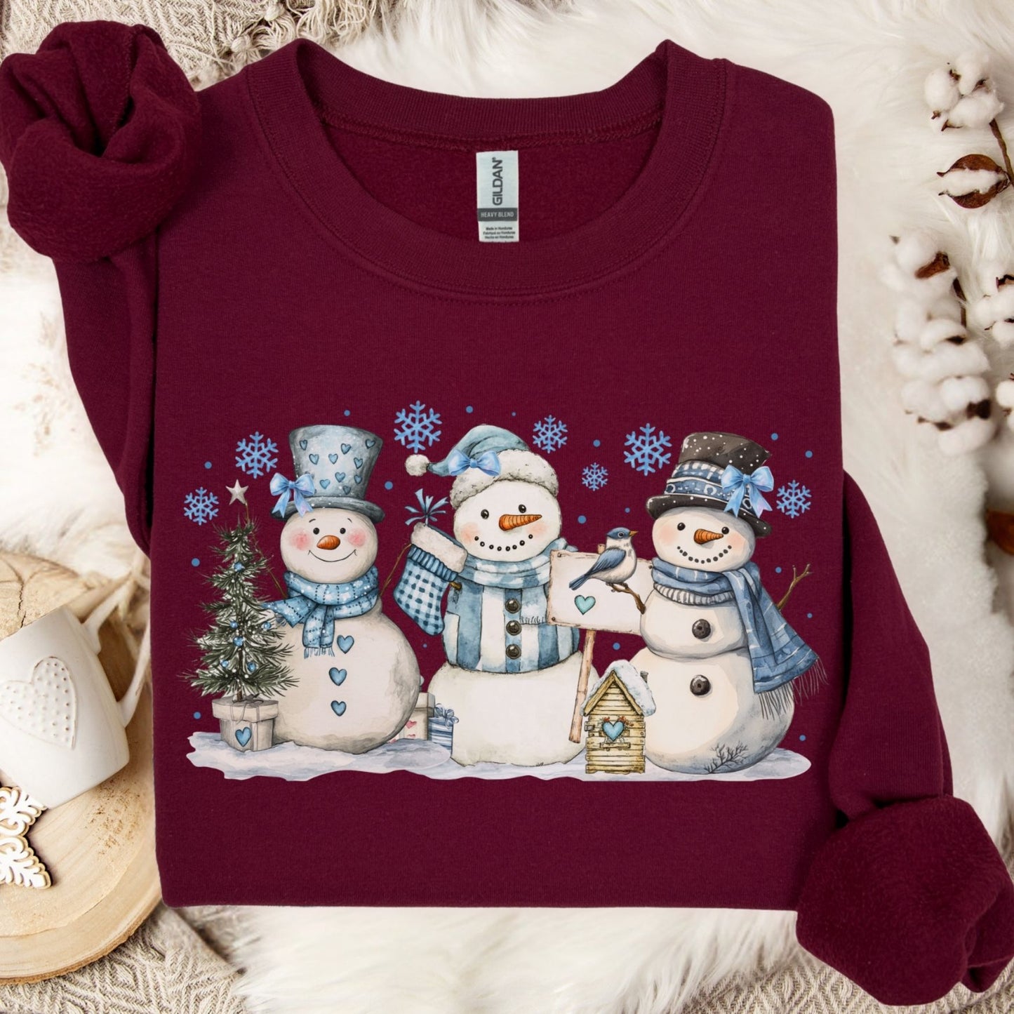Maroon heavy blend sweatshirt with watercolor woodland snowmen, blue hats, scarves, birdhouse, and birds.