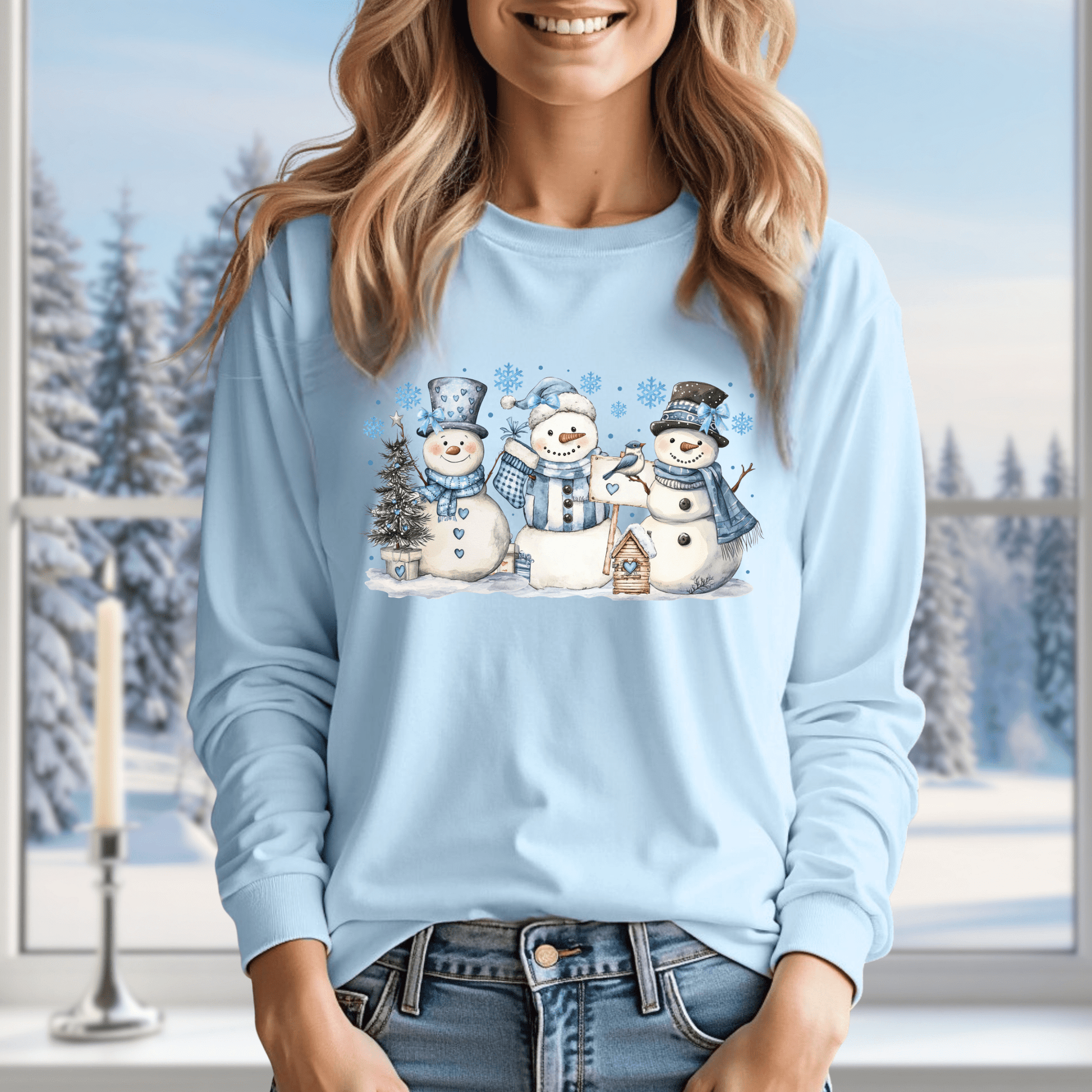 Light blue long sleeve tee with watercolor snowmen, blue hats, scarves, and a birdhouse.