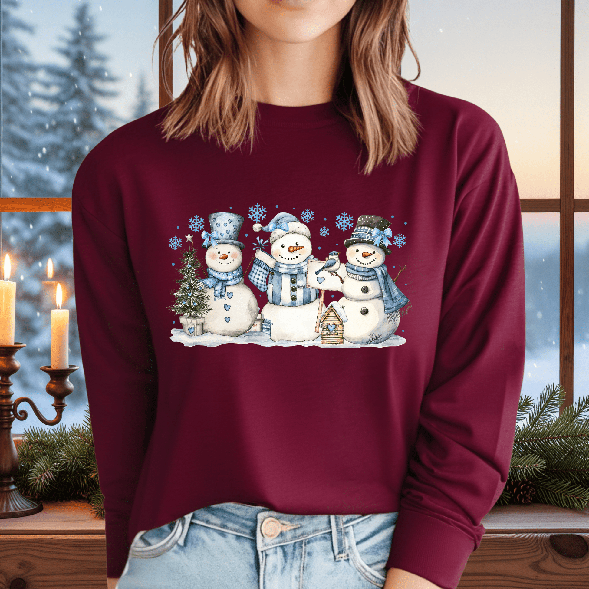 Maroon long-sleeve tee with three watercolor snowmen, blue hats/scarves, and a birdhouse.