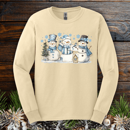 Beige long-sleeve tee with watercolor snowmen, blue hats/scarves, birdhouse, and snowflakes.