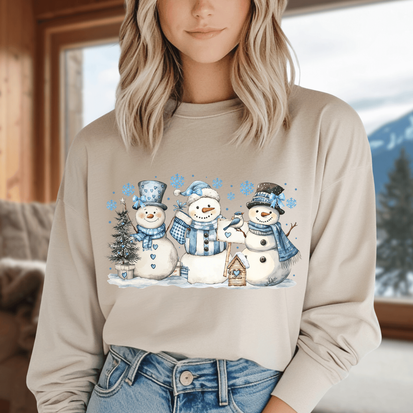 Beige long-sleeve tee with watercolor snowmen, blue hats, scarves, and snowflakes.