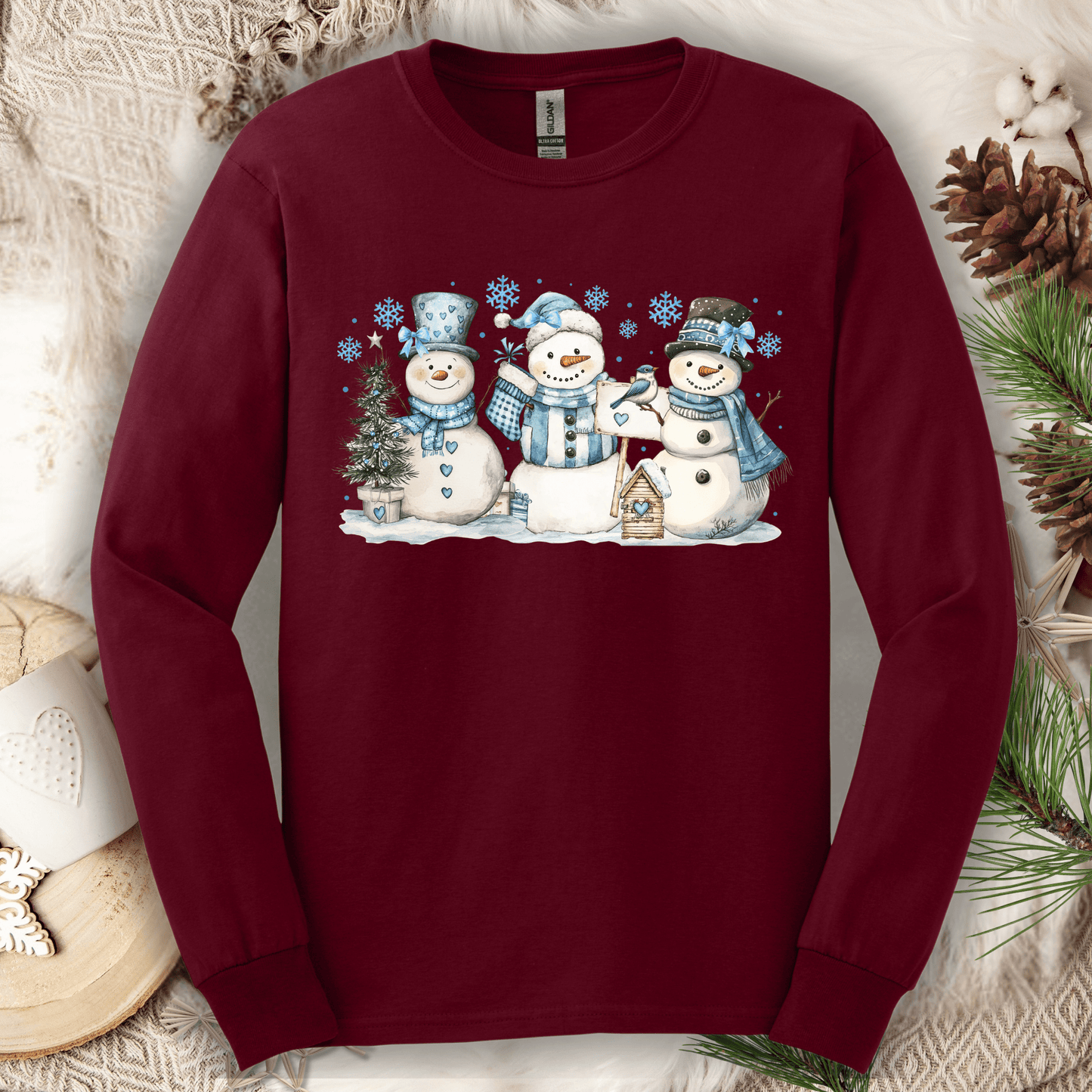 Maroon long sleeve tee with watercolor snowmen, blue hats/scarves, birdhouse, and snowflakes.